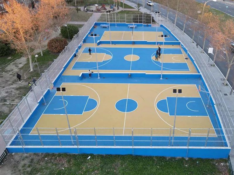 Instalación deportiva exterior con pavimento deportivo azul y beige, rodeadas de valla de seguridad.